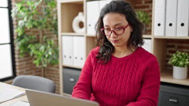 Young beautiful hispanic woman business worker using laptop with doubt expression at office