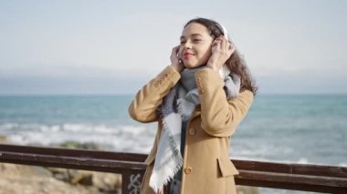Genç ve güzel İspanyol kadın deniz kenarında müzik dinliyor ve dans ediyor.
