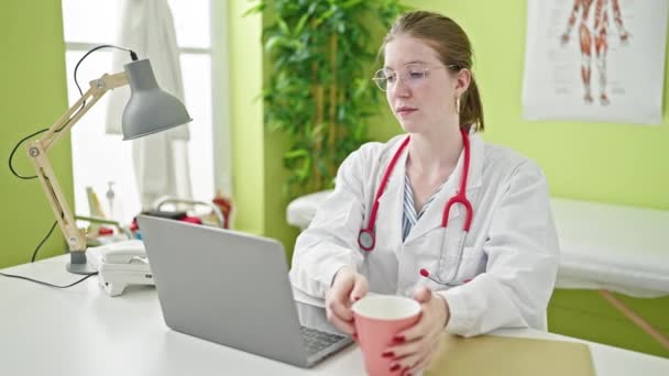 年轻的金发女医生在诊所用笔记本电脑喝咖啡 — 图库视频影像