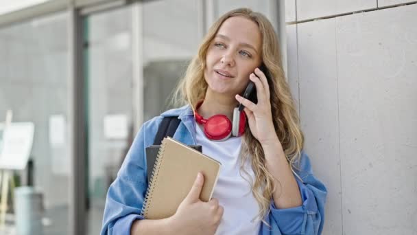在大学里 年轻的金发女学生拿着用智能手机聊天的书 — 图库视频影像