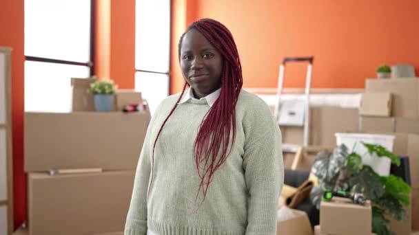新しい家で自信を持って立って笑みを浮かべて編組髪を持つアフリカの女性 — ストック動画