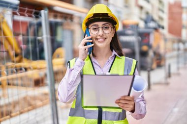 Genç İspanyol kadın mimar, caddede akıllı telefon okuyarak konuşuyor.