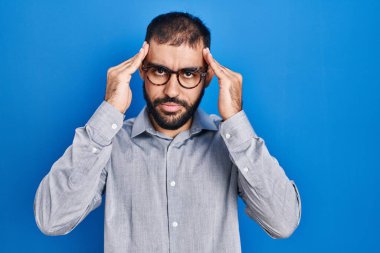 Mavi arka planda sakallı, başı ağrıyan orta doğulu bir adam. Stres yüzünden. migren ağrısı. 