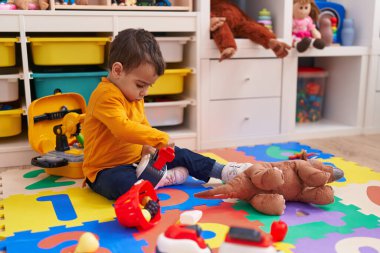 Anaokulunda yerde oturmuş süpermarket oyunu oynayan sevimli İspanyol çocuk.