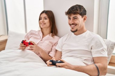 Mand and woman couple playing video game sitting on bed at bedroom