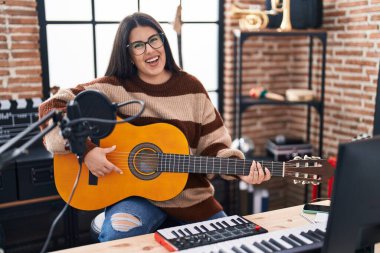 Young hispanic woman musician playing spanish guitar at music studio