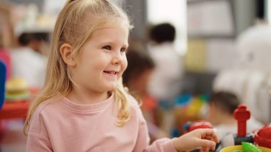 Sevimli sarışın kız, gülümsüyor. Anaokulunda oynarken kendine güveniyor.