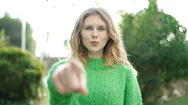 Young blonde woman smiling confident pointing with finger at park