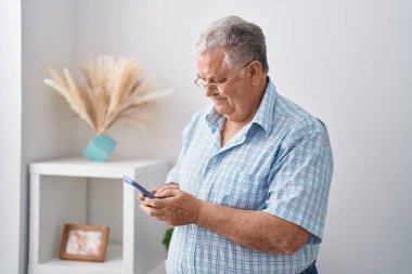 Middle age grey-haired man using smartphone standing at home