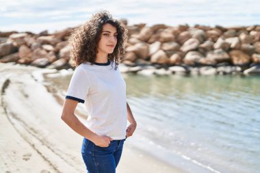 Young hispanic woman smiling confident looking to the side at seaside