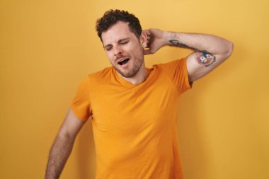 Sarı arka planda dikilen genç İspanyol adam yorgun ve rahat, uykulu ve sabahın erken saatleri için esniyor. 