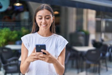 Kahve dükkanının terasında akıllı telefon kullanan, kendine güvenen, güzel İspanyol bir kadın.