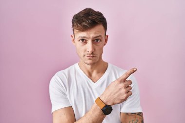 Pembe arka planda duran beyaz bir adam, elini kenarı işaret ediyor, ciddi ve sakin bir yüz ifadesi sergiliyor. 