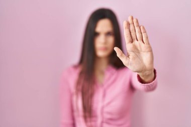 Pembe arka planda duran genç İspanyol kadın avucunun içi gibi şarkı söylemeyi kesiyor. Yüzünde olumsuz ve ciddi bir jest olan uyarı ifadesi. 