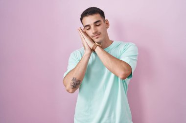 Yakışıklı İspanyol adam pembe arka planda ayakta uyur. Yorgun düşler kurar, elleriyle poz verir ve gözleri kapalı gülümserdi.. 