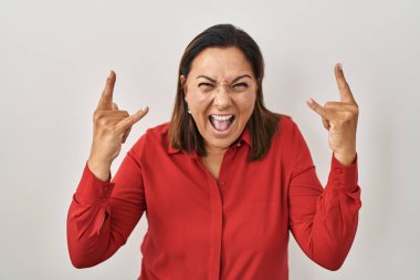 Beyaz arka planda dikilen Latin kökenli olgun bir kadın çılgın bir ifadeyle elleri havada rock sembolü yapıyor. Müzik yıldızı. ağır kavram. 