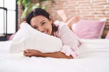 Young hispanic woman hugging pillow lying on bed at bedroom