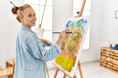 Beyaz kadın sanatçı, resim stüdyosunda kendine güvenen gülümsüyor.