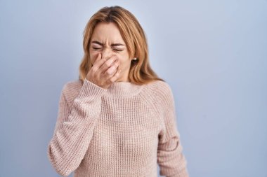 Mavi arka planda dikilen İspanyol kadın pis ve iğrenç bir koku alıyor. Nefesini burnunda tutuyor. Kötü kokuyor. 