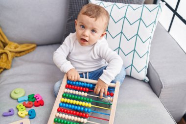 Abaküsle oynayan sevimli sarışın çocuk evdeki kanepede oturuyor.