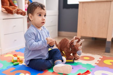 Anaokulunda rahat bir ifadeyle yerde oturan sevimli İspanyol çocuk.