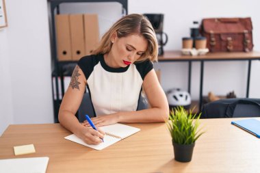 Genç, güzel İspanyol iş kadını ofiste deftere yazı yazıyor.