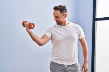 Spor merkezinde dambıl eğitimi alarak gülümseyen beyaz bir genç.