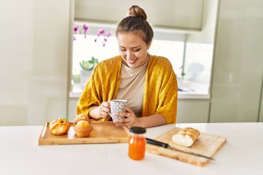 Young beautiful hispanic woman having breakfast drinking coffee at the kitchen