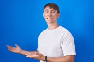 Mavi arka planda duran beyaz tenli sarışın adam gülümseyerek içeri girmeye davet ediyor. 