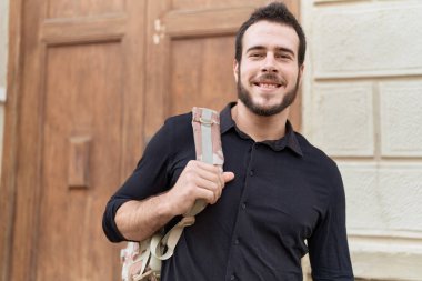 Young hispanic man smiling confident wearing backpack at street