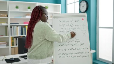 Örgü örmüş saç öğretmeni olan Afrikalı kadın üniversite kütüphanesinde matematik dersi veriyor.