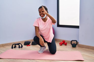 Spor kıyafetleri ve güvenlik maskesi takan genç Afro-Amerikan spor salonunda mutlu mesut gülümsüyor. 
