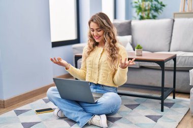 Genç bir kadın evde yerde oturmuş video görüşmesi yapıyor.