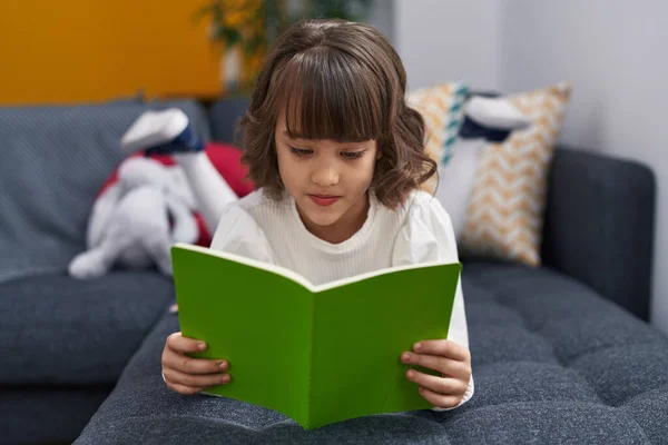 Adorable Hispanic Girl Reading Book Lying Sofa Home — Stockfoto