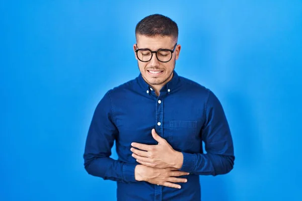 Mladý Hispánec Nosí Brýle Nad Modrým Pozadím Rukou Břiše Protože — Stock fotografie