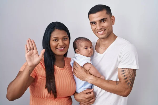 孤立した背景の上に一緒に立って赤ちゃんを持つ若いヒスパニック系のカップルはこんにちは幸せと笑顔 優しい歓迎ジェスチャーを言って放棄 — ストック写真