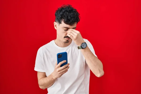 Spaanse Man Met Behulp Van Smartphone Rode Achtergrond Moe Wrijven — Stockfoto