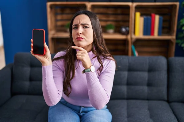 Młoda Brunetka Kobieta Trzyma Smartfon Pokazując Pusty Ekran Poważny Twarz — Zdjęcie stockowe