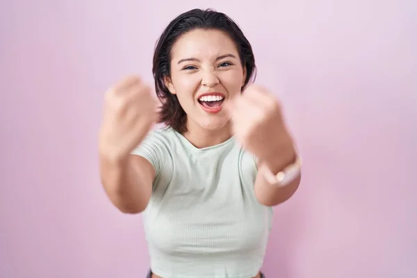 ピンク色の背景に立っているヒスパニック系の若い女性は怒りで叫んでいる間 怒りと怒りの拳を上げる怒っている 怒りと攻撃的な考え方 — ストック写真