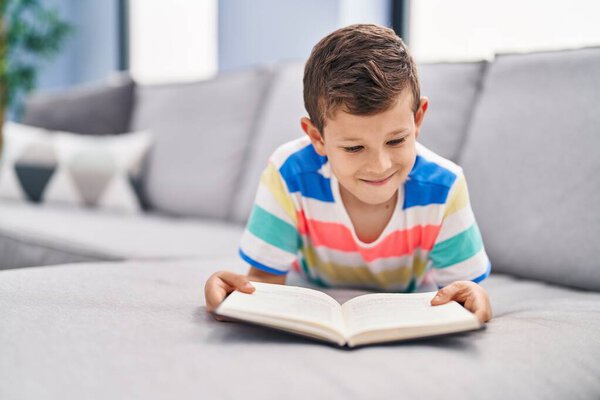 Blond child reading book sitting on sofa at home