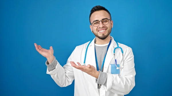 Latynoski Mężczyzna Lekarz Uśmiecha Się Pewnie Prezentując Odizolowanym Niebieskim Tle — Zdjęcie stockowe