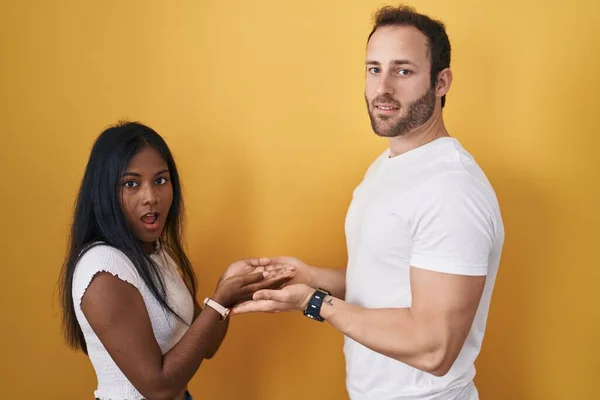 Interracial Couple Standing Yellow Background Pointing Aside Hands Open Palms — Stock Photo, Image
