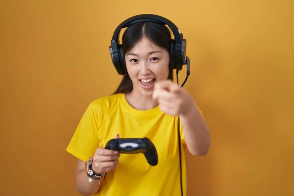 中国年轻女子正在玩电子游戏 手里拿着控制器 用手指指着你和相机 笑得正正正经经 — 图库照片
