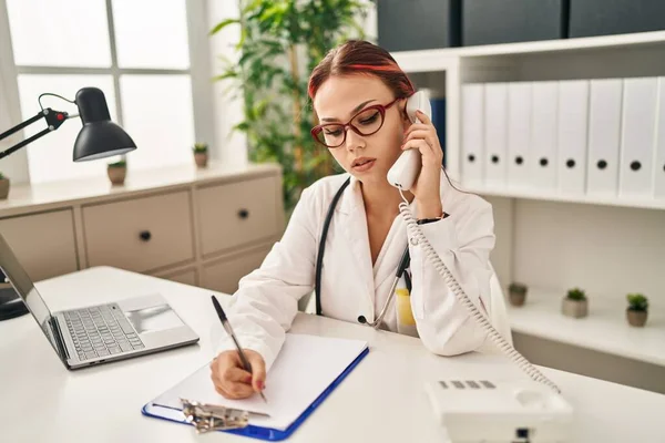 Genç beyaz kadın doktor klinikte telefon yazısıyla konuşuyor.