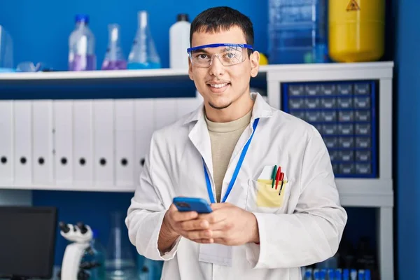 研究室でスマートフォンを使って自信を持って笑っている若い男科学者 — ストック写真