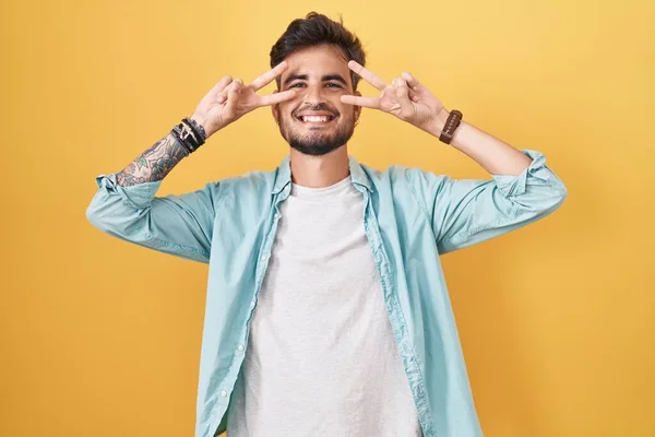 Mladý Hispánec Tetováním Stojí Nad Žlutým Pozadím Dělá Mírový Symbol — Stock fotografie