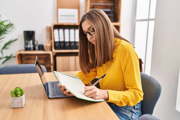 利用在办公室工作的笔记本电脑在账面上写作的女青年 — 图库照片
