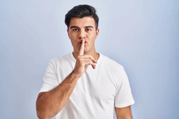 ヒスパニック系の男性の青の背景の上に唇に指で静かにするように求めて立っている 沈黙と秘密の概念 — ストック写真