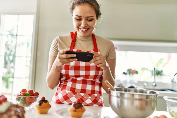 年轻美丽的惊慌失措的女人笑着自信地用智能手机在厨房里给蛋糕拍照 — 图库照片