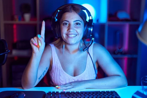 年轻的金发女人带着耳机玩电子游戏 带着第一指尖 面带微笑 自信而快乐 — 图库照片